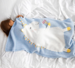 un enfant sur un drap blanc froissé qui dort avec un plais bleu avec une licorne blanche