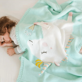 Petite fille aux cheveux bouclés dormant sur un drap blanc avec un plaid vert avec une licorne blanche