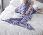 Plaid sirène tricoté violet sur lit blanc avec un bras