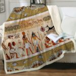 Plaid à motif et symboles égyptiens dans les tons marrons étendu sur un canapé blanc avec livre et tasse posée sur le dessus