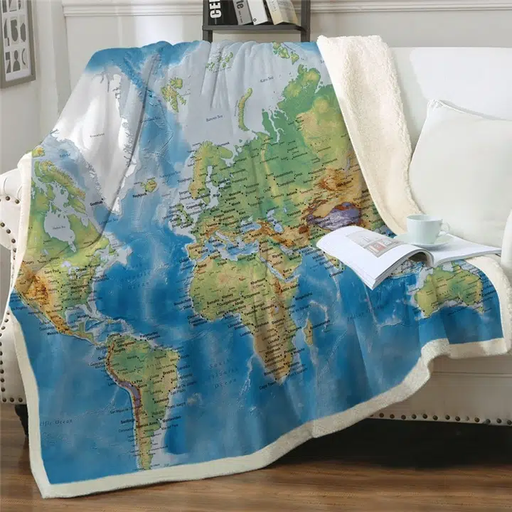 Dans un coin salon lumineux et clair, on voit un plaid imprimé carte du monde posé sur un canapé blanc.