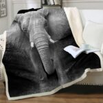 Dans un salon avec du parquet et des murs avec moulures blanches, on voit un plaid éléphant posé sur un canapé blanc. Le fond du plaid est noir.