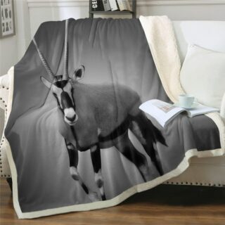 Dans un coin salon agréable et lumineux, on voit un plaid gris à l'imprimé gazelle posé sur un canapé blanc.