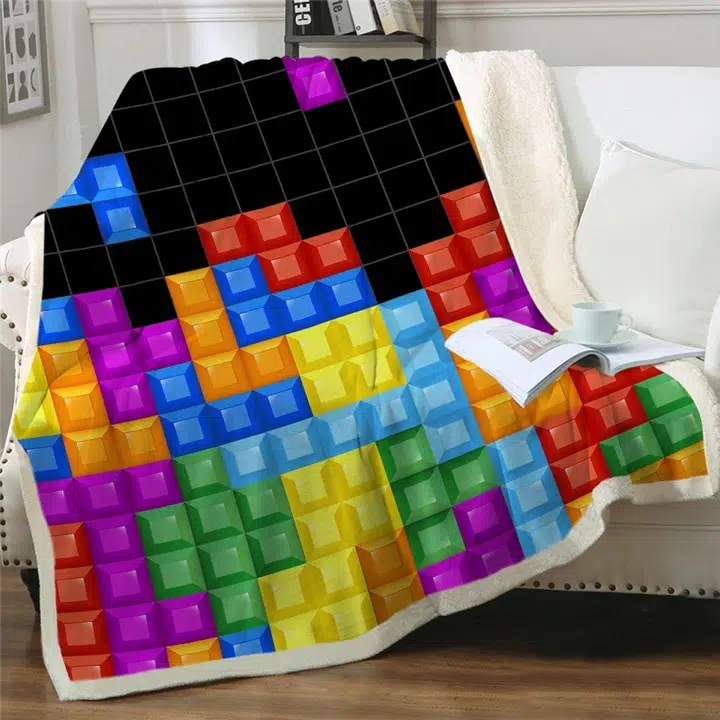 Plaid à fond noir avec carré multicolores du jeu Tetris posé sur un canapé blanc