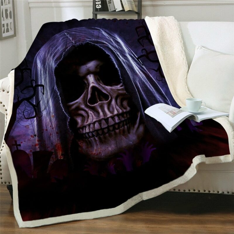 Plaid noir style gothique avec une tête de mort portant une capuche violette. Le plaid est étendu sur un canapé blanc et déborde sur le sol en parquet marron. Il y a un livre ouvert dessus avec une tasse blanche posée dessus.