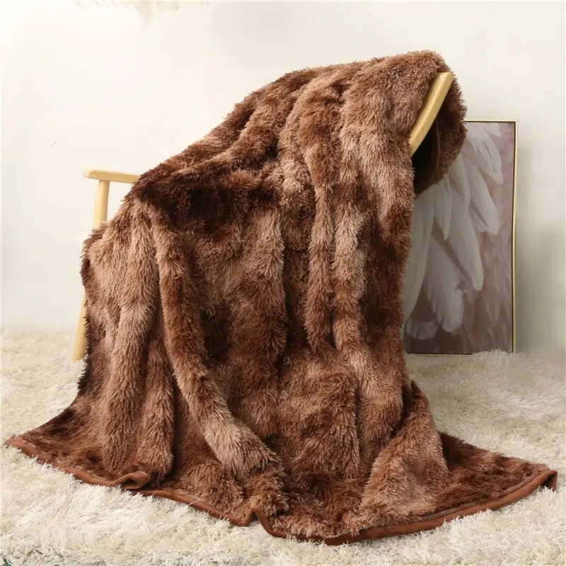 Un plaid en fourrure marron recouvrant une chaise posée sur un tapis à poils longs beige. Il y a un cadre au fond beige avec des ailes blanches, posé par terre conte le mur.