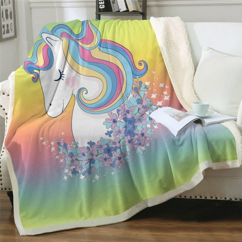 Dans le coin d'un salon lumineux, sur un canapé, on voit un plaid multicolore à l'effigie d'une licorne à la crinière multicolore.