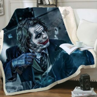 Plaid bleu sombre avec imprimé Joker 3D avec une lame dans sa main ganté sur un canapé blanc et débordant sur le parquet marron. Il y a un livre ouvert dessus avec une tasse banche par dessus.