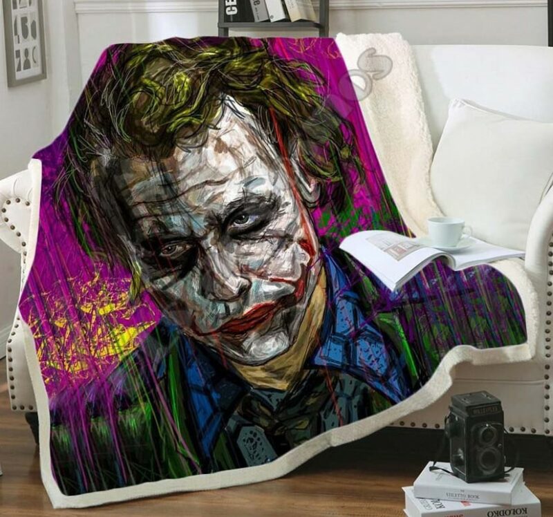 Plaid multicolore imprimé tête du Joker sur un canapé blanc et débordant sur le sol en parquet marron.
