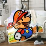 Plaid avec dessin du personnage de Mario Bros dans des tons orangé. Le plaid est étendu sur un canapé blanc à côté d'un coussin blanc dans un décor de salon.