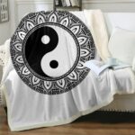 Plaid noir et blanc confortable avec symbole Yin et Yang sur un canapé blanc débordant sur le sol en parquet marron. Il ya un livre ouvert dessus avec une tasse blanche par dessus et un coussin blanc à côté.