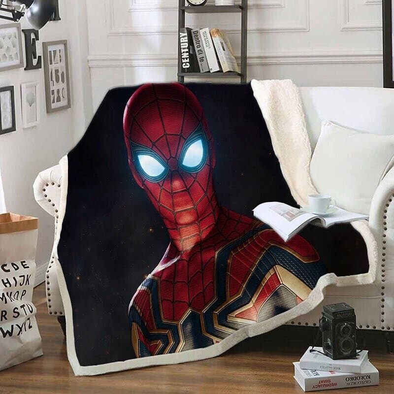 Plaid polaire noir avec visage de Spiderman en cagoule avec les yeux bleu brillants . Ce plaid est étendu sur un canapé blanc dans un décor de salon avec étagères et cadres au mur.