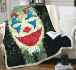Plaid polaire coloré confortable à motif Joker clown sur un canapé blanc et débordant sur le sol en parquet marron. Il y a un livre ouvert posé dessus avec une tasse blanche par dessus et un coussin blanc à côté.