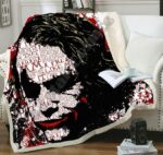 Plaid polaire rouge et noir avec motif tête de Joker et écritures sur le visage, étendu sur un canapé blanc et débordant sur le sol en parquet marron.