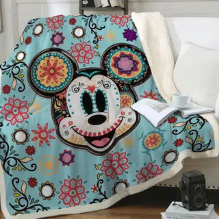 Plaid avec la tête de Mickey avec rosaces et dessins tribaux colorés étendu sur un canapé blanc à côté d'un coussin blanc .