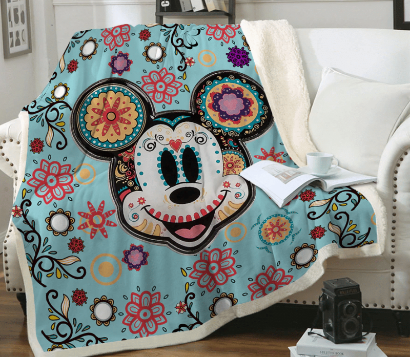 Plaid avec la tête de Mickey avec rosaces et dessins tribaux colorés étendu sur un canapé blanc à côté d'un coussin blanc .