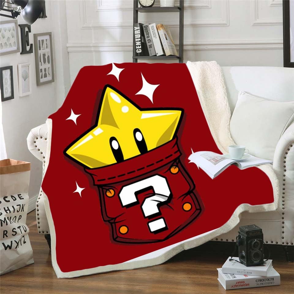 Un plaid rouge avec l'étoile jaune de Mario dans un sac avec point d'interrogation. Il est étendu sur un canapé blanc à côté d'un coussin blanc dans un décor de salon.