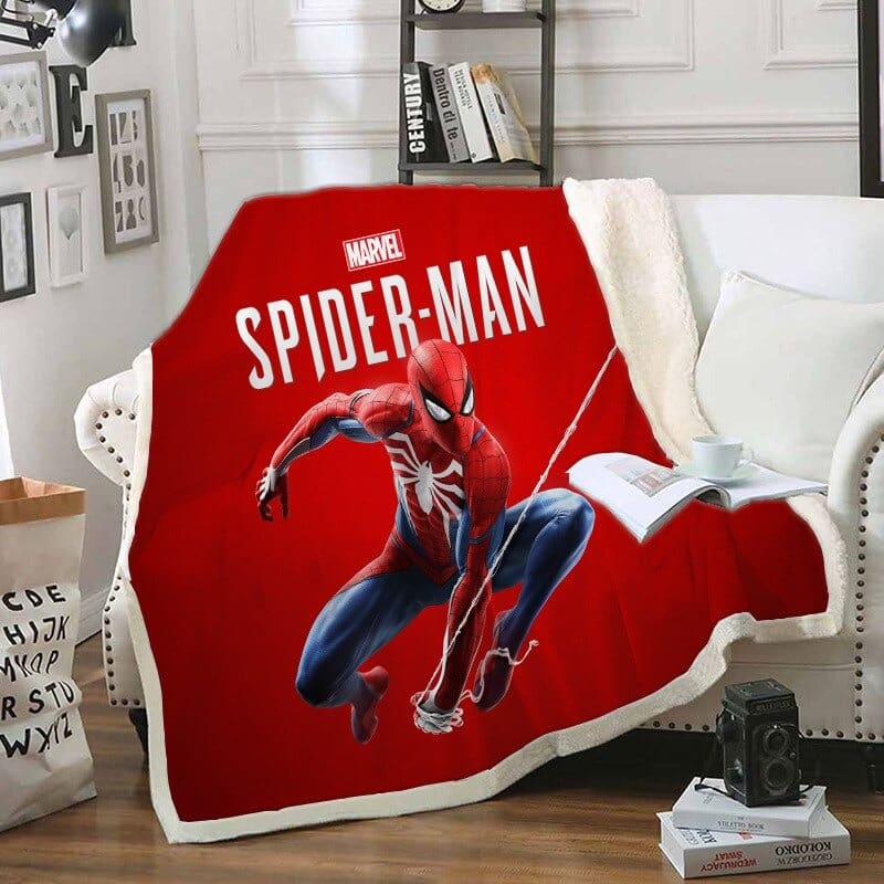 Plaid en polaire rouge avec Spiderman écrit et le personnage en plein action. L e plaid est étendu sur un canapé blanc dans un décor de salon.
