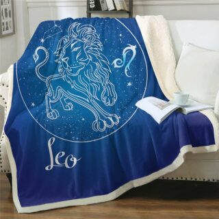 Plaid polaire bleu nuit signe astrologique lion sur un canapé blanc. Il y a un livre ouvert posé dessus avec une tasse blanche par-dessus.