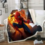 Plaid polaire coloré avec Spiderman dans une explosion. Le plaid est étendu sur un canapé blanc dans un décor de salon avec étagère et cadres au mur.