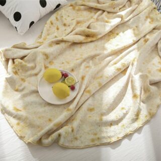 plaid beige tacheté de jaune avec assiette de fruits dessus sur un sol blanc avec un coussin à pois noir et blanc sur le coté