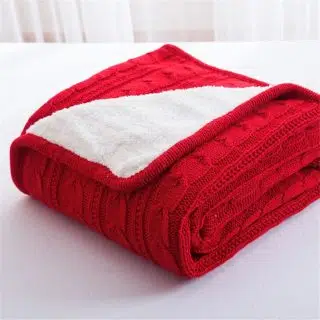 Plaid rouge en tricot avec maille torsadée plié avec un revers pour visualiser un intérieur blanc en polaire.