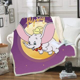 Plaid violet avec Dumbo qui vole devant le soleil. Le plaid est étendu sur un canapé blanc à côté d'un coussin blanc. avec une tasse sur un livre posée dessus. Des livres sont sur le sol en parquet avec un appareil noir dessus.