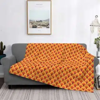 Plaid polaire vintage à trois nuances de orange avec motifs arrondis retro étendu sur un canapé gris dans un décor de salon. Le sol est un tapis beige au style bohème à rayures , il y a un cadre avec un paysage de nature au -dessus du canapé, un objet de déco en macramé accroché à coté et un petit cactus à l'opposé.