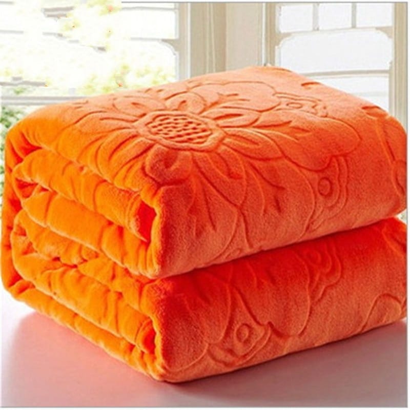 Couvre lit orange plié avec fleurs tournesols gravées dessus, posé sur une table avec une fenêtre en arrière-plan.