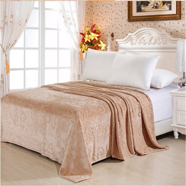 Dans une chambre au décor rustique, une grande couverture beige douce avec motifs arabesques utilisée comme un couvre-lit recouvrant un lit 2 places avec literie blanche.