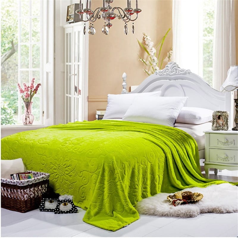 Dans une chambre au décor baroque, une grande couverture verte pomme douce avec motifs arabesques utilisée comme un couvre-lit recouvrant un lit 2 places avec tête de lit blanche à moulure avec literie blanche. Il y a un tapis en fourrure blanc au pied du lit et des paniers en osier.