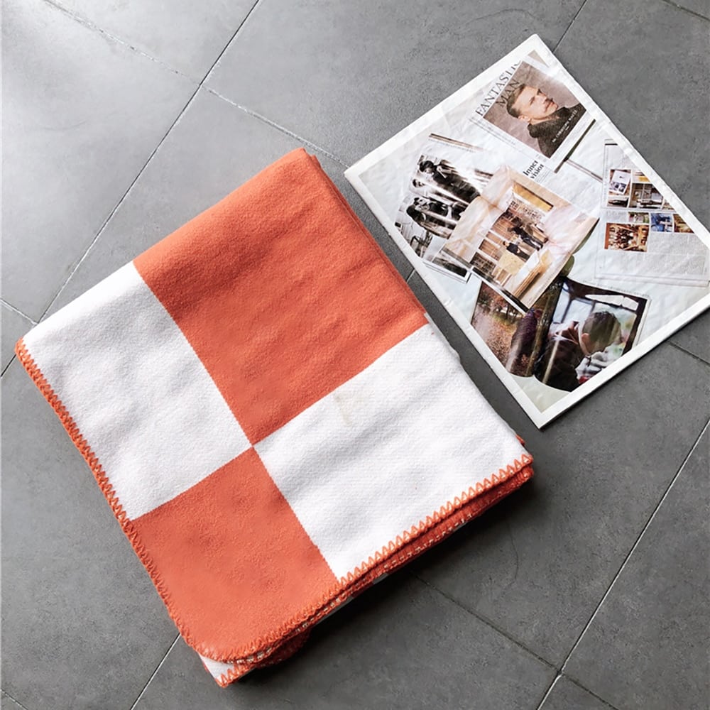 Couverture en damier blanc et orange avec coutures apparentes sur les bordures plié sur un sol gris à coté d'une page de magazine.