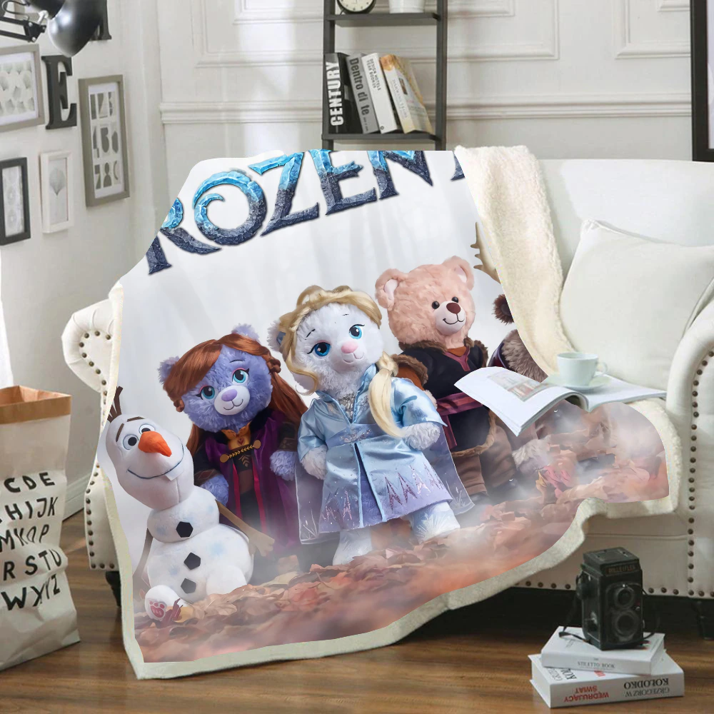 Plaid polaire avec oursons déguisés en personnages de la Reine des neiges. Le plaid est étendu sur un canapé blanc dans un décor de salon.