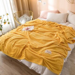 Plaid polaire jaune côtelé étendu sur un lit 2 places à la literie blanche. La chambre est cosy avec des murs en beige.