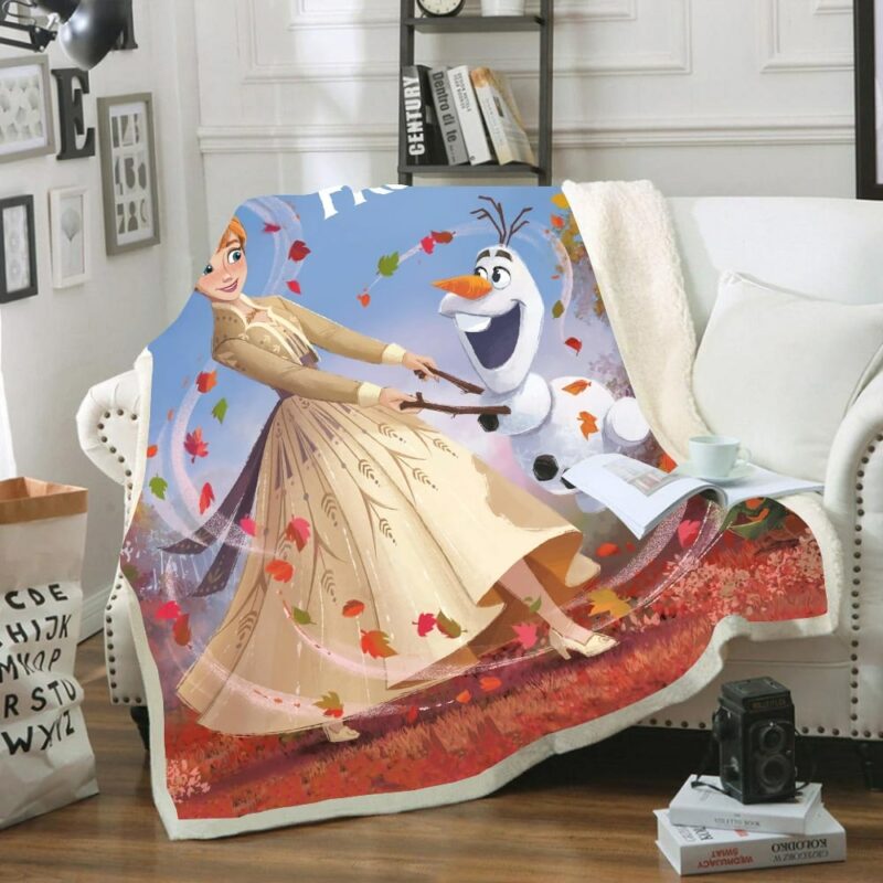 Plaid en polaire multicolore avec les personnages de Olaf et Ana adulte de la Reine des neiges dansant et tournoyant dans les feuilles d'automne. Le plaid est étendu sur un canapé blanc dans un décor de salon.