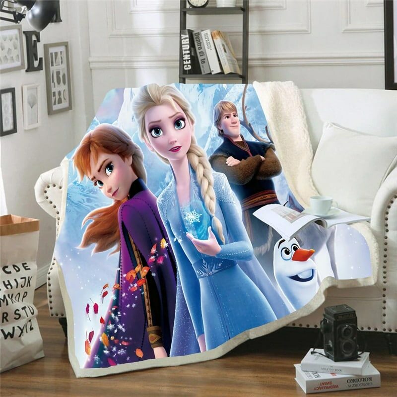 Plaid polaire coloré avec les personnages de la Reine des neiges :Elsa, Ana, Olaf et Kristoff. Le plaid est étendu sur un canapé blanc dans un décor de salon avec parquet en bois marron au sol.