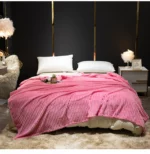 Couverture rose en velours côtelé étendu sur un lit deux places avec deux coussins blanc dans une chambre au mur noir avec lignes dorés. Le décor est cocooning avec un tapis en fourrure beige et des petites lampes de chevet en plumes.