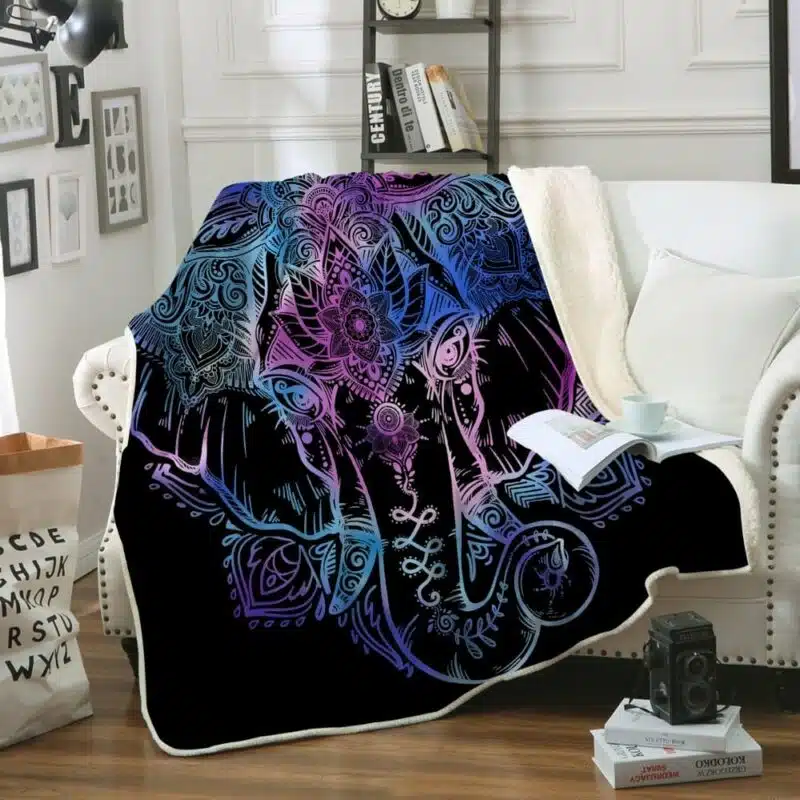 Dans un salon avec des murs blancs et des moulures, on voit un canapé blanc recouvert d'un plaid noir avec une grosse tête d'éléphant de toutes les couleurs.