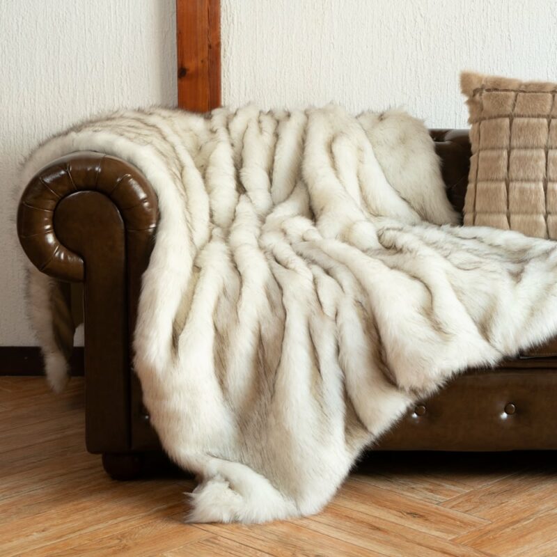 Plaid en fausse fourrure blanc étendu sur un canapé club marron à côté d'un coussin marron quadrillé dans un salon au parquet marron