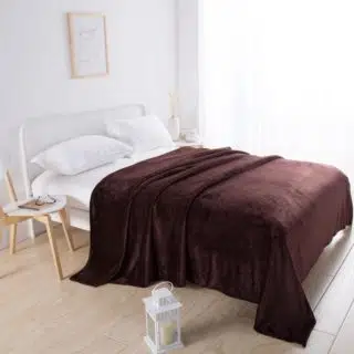 Plaid en velours marron couvrant un lit dans une chambre blanche au sol beige avec chaise en bois et lanterne blanche sur le sol