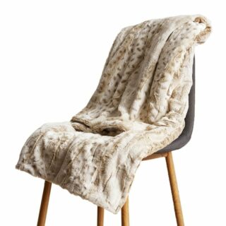 Plaid léopard beige clair en fourrure plié en 2 étendu sur une chaise scandinave avec pieds obliques en bois.