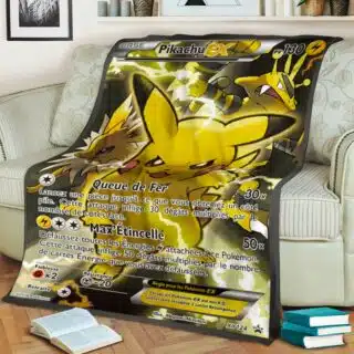 Plaid carte Pokémon Pikachu EX noir et jaune étendu sur un canapé beige avec fleurs et rayures. Il y a une pile de 3 livres et un livre ouvert sur le sol en parquet.