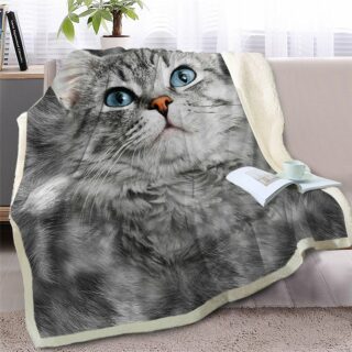 Plaid avec motif de chat gris aux yeux bleus posé sur un canapé gris avec un livre et une tasse à café dessus