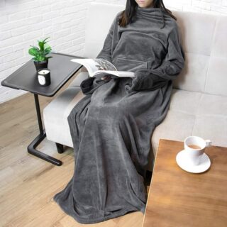 Plaid à manche longue porté par une personne assise sur un canapé gris en train de lire avec une tasse à café posée sur une table en bois