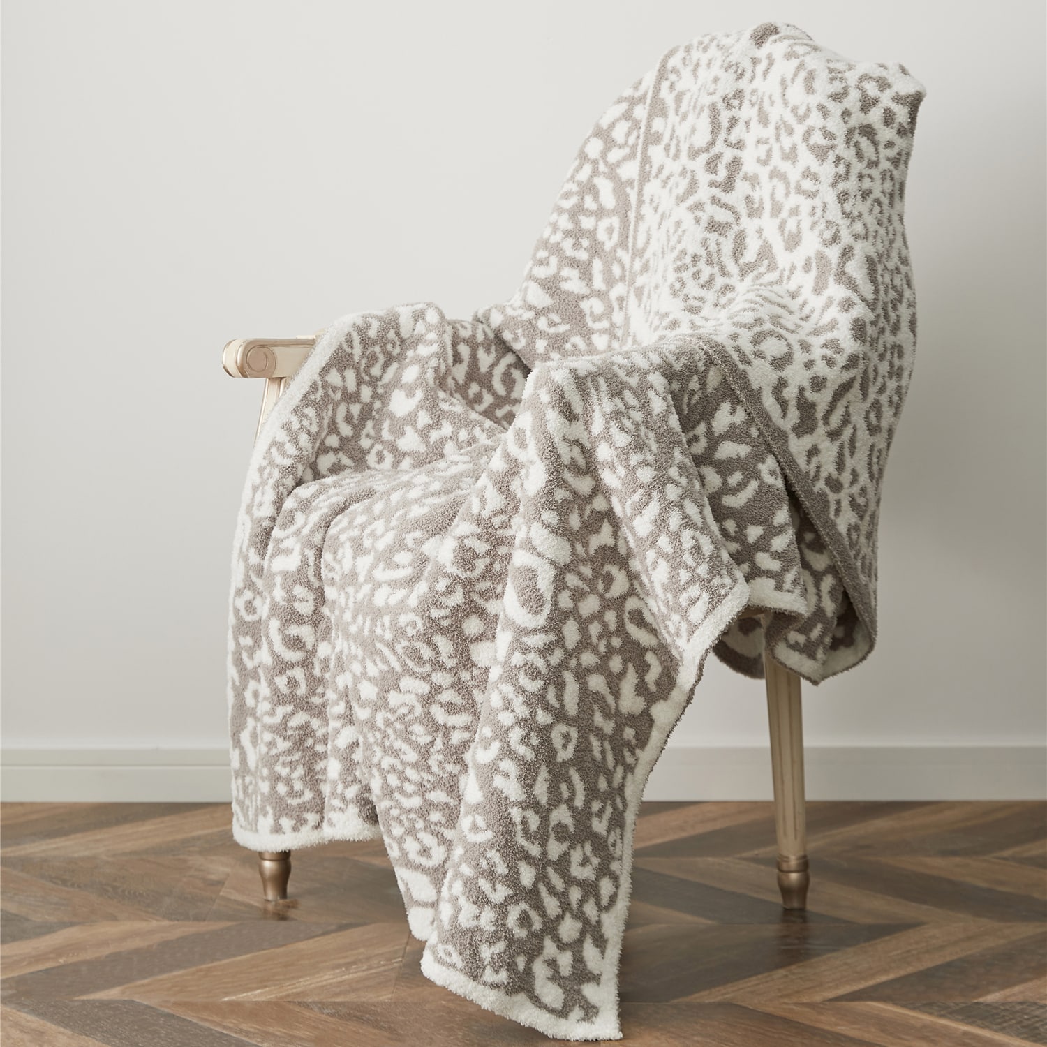 Plaid léopard de couleur gris et blanc posé sur une chaise avec du parquet et devant un mur blanc