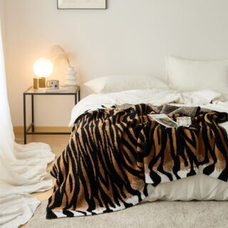 Plaid en motif léopard de couleur blanc marron et noir, posé sur un lit aux draps blanc avec un tapis de couleur blanc cassé