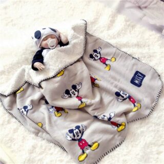 Plaid avec des motifs de Mickey posé sur un bébé dormant avec un bonnet et sur une couverture blanche