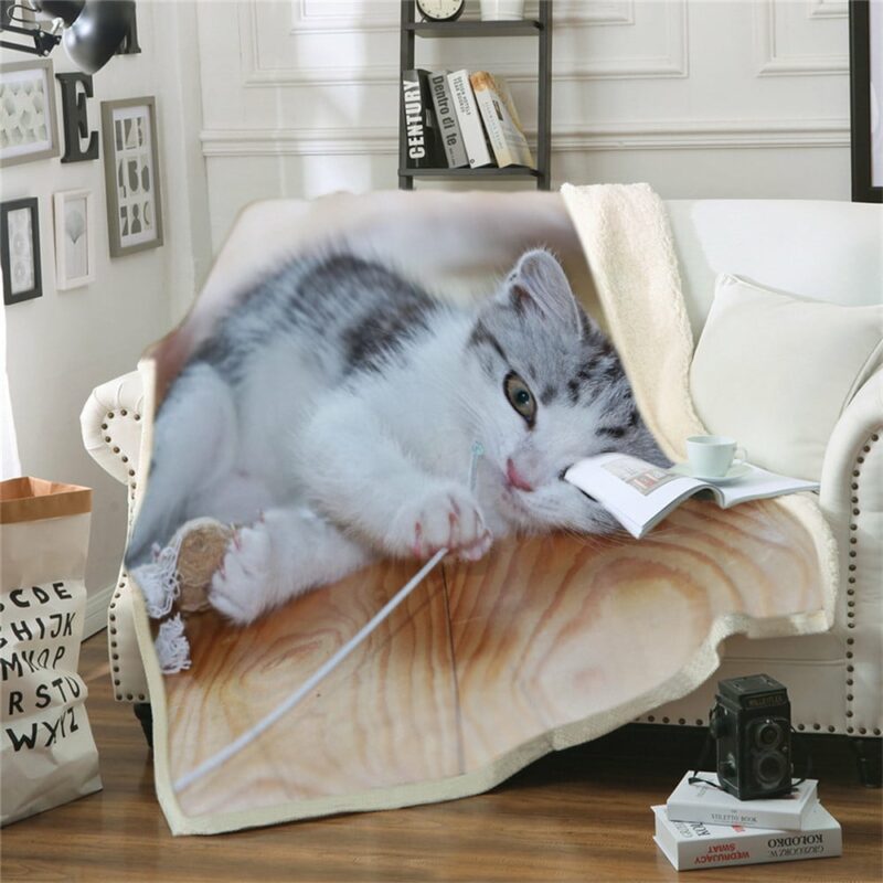 plaid posé sur un canapé blanc avec un joli imprimé de chaton en train de jouer avec un fil de laine