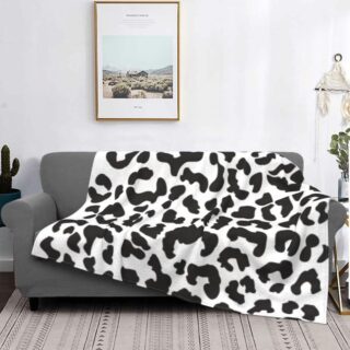 canapé gris dans un salon avec un plaid au motif léopard blanc, avec un tableau au dessus