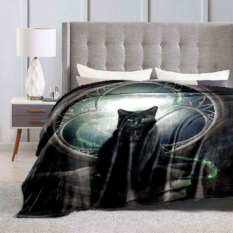 sur un lit avec une tête de lit grise, près d'une table de chevet, est installé un grand plaid avec le dessin d'un chat noir avec un symbole mystique